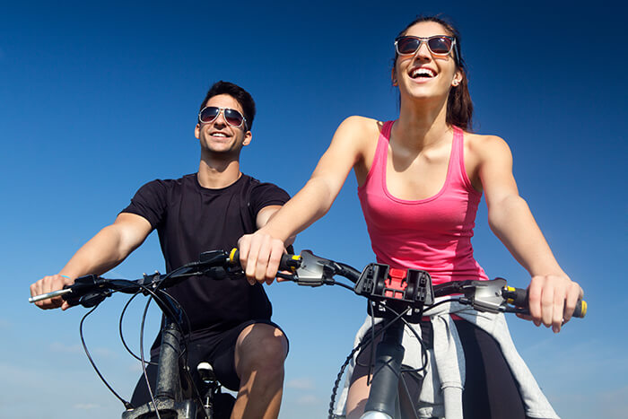 Casal jovem, formado por homem e mulher brancos, sorrindo ao andar de bicicleta