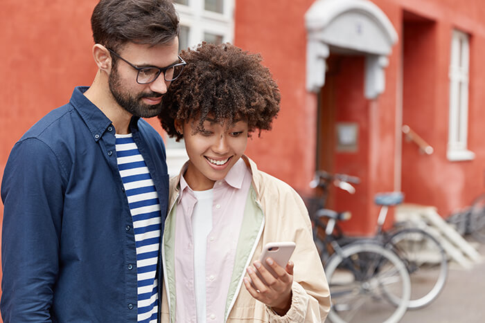 Casal interacial jovem olhando para o celular durante passeio na rua